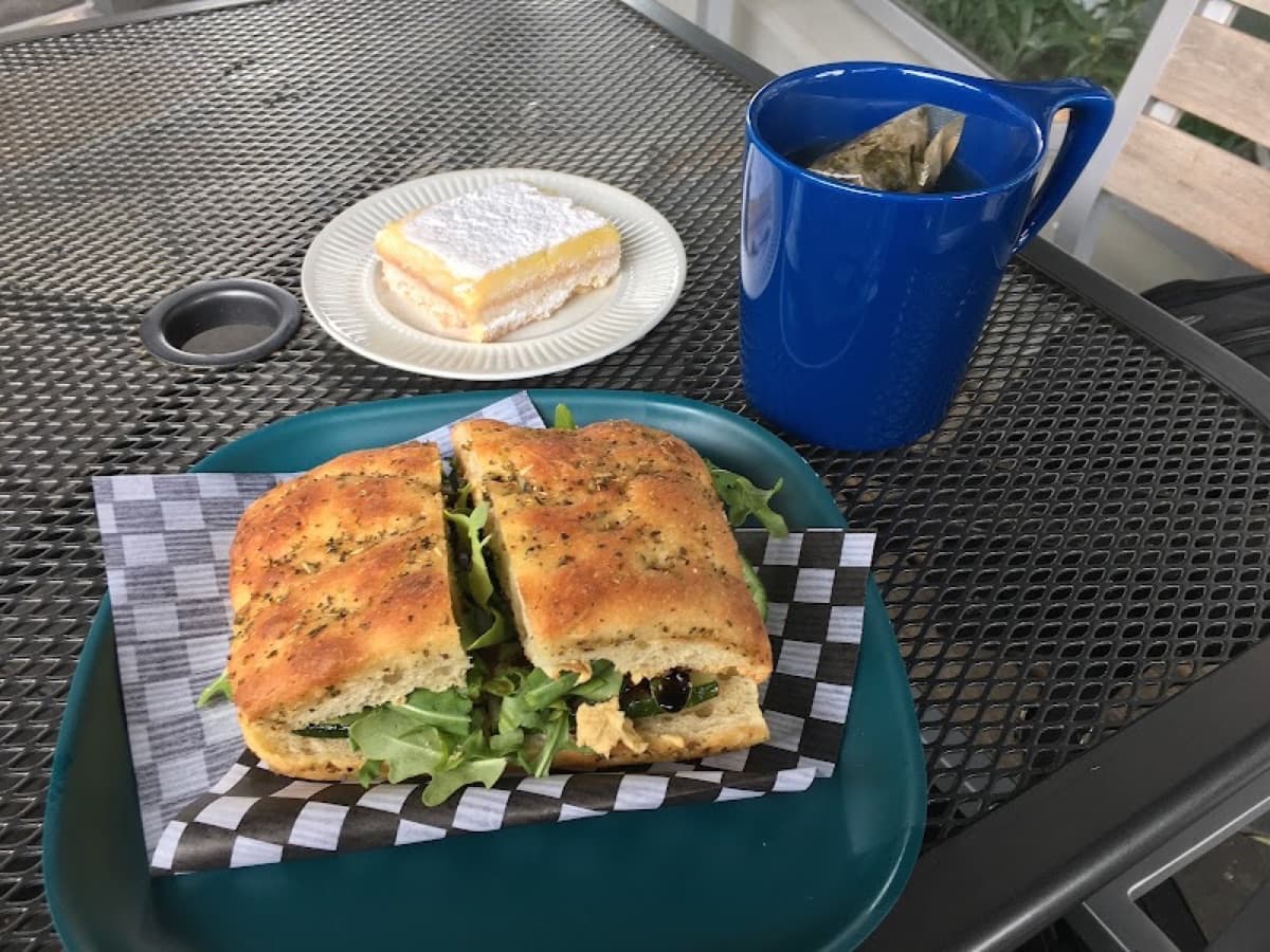 House focaccia sandwich with arugula, a lemon bar, and tea on the patio table
